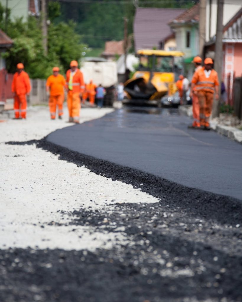 Fresh asphalt along a street with paving equipment and workers in orange safety clothing