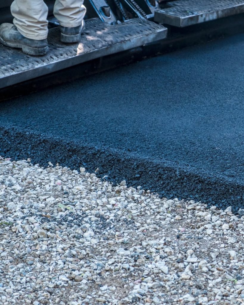 Close-up of paving equipment laying dark asphalt over a gravel base